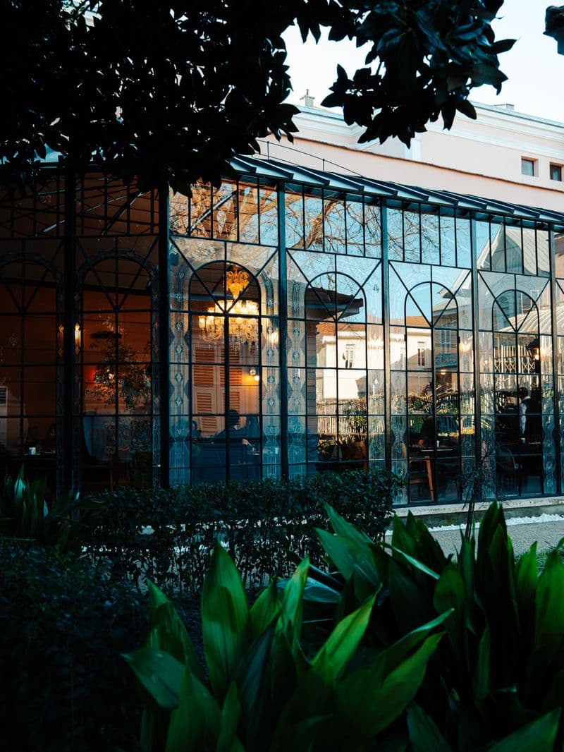 Elegant glass conservatory with dark iron frames and warm interior lighting